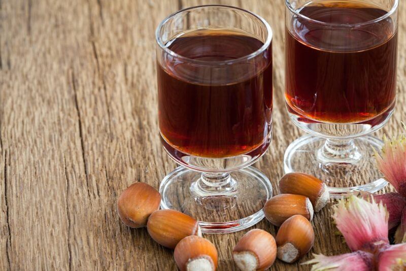 Two glasses of hazelnut liqueur on a table with hazelnuts scattered around