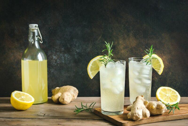 Two glasses of homemade ginger ale with ice, with a bottle of the ginger ale on a table