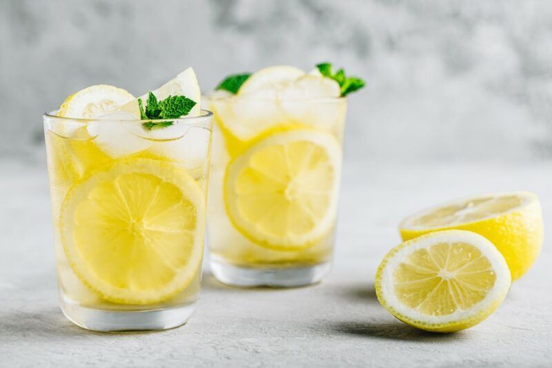 Two glasses of honey whiskey lemonade, with slices of lemon and ice, next to a lemon