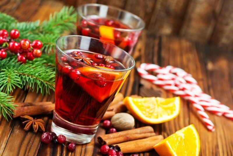 Two glasses of hot cranberry cider on a table with citrus wedges and spices