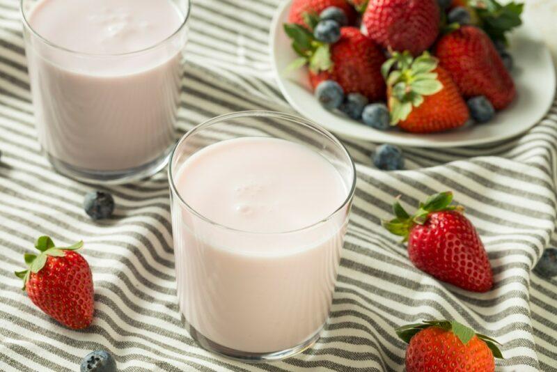 A striped cloth with two glasses of kefir, some strawberries and blueberries, plus a bowl of strawberries and blueberries