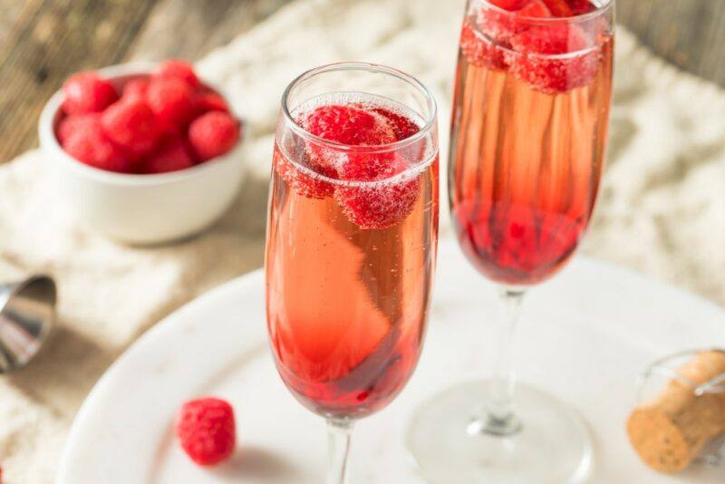 Two champagne glasses containing a kir royale cocktail and fresh berries, next to a white container of fresh berries