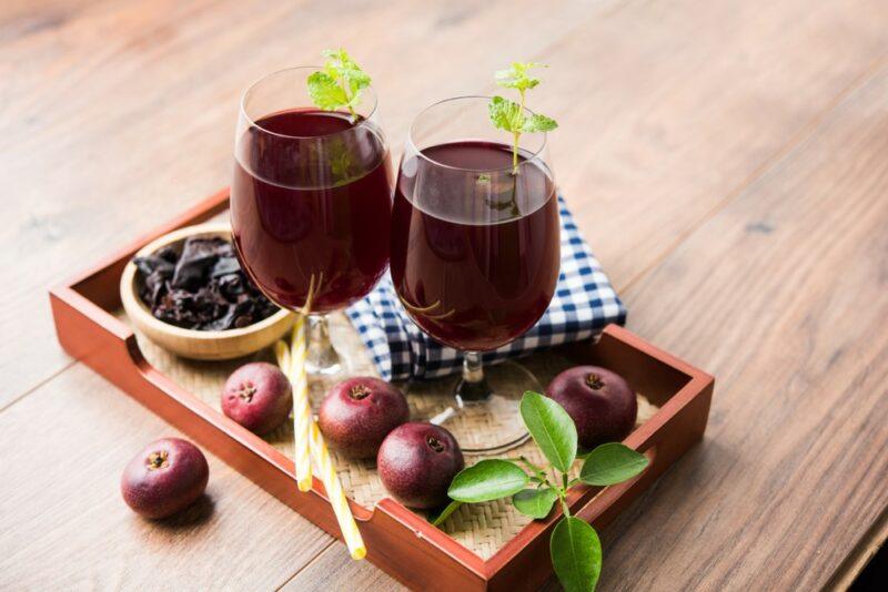 A wooden board with two glasses of kokum sherbet, with a bowl of the fruit and individual pieces of kokum fruit