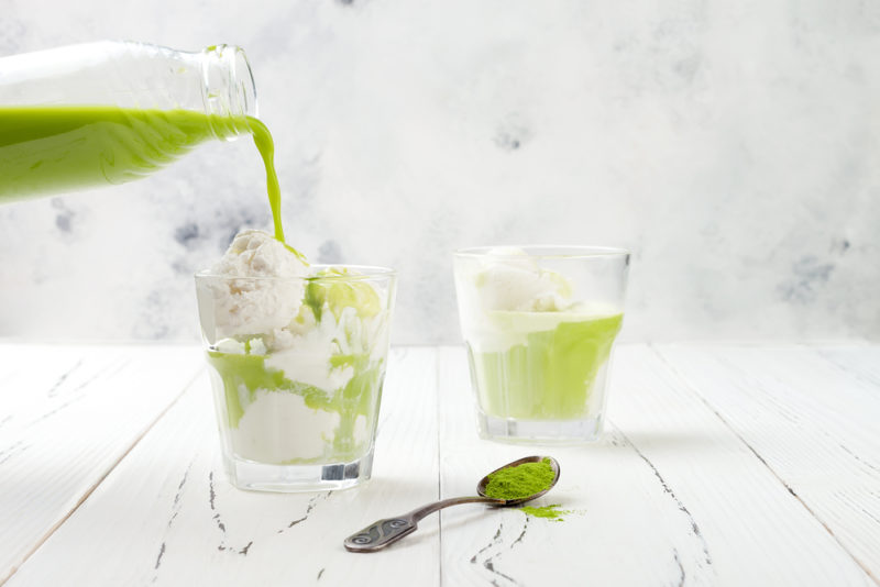 Two glasses of vanilla ice cream with matcha green tea being poured over top