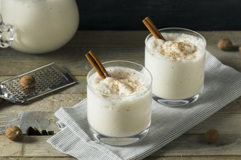 Two glasses of a milk punch cocktail on a cloth, with cinnamon sticks used as a garnish