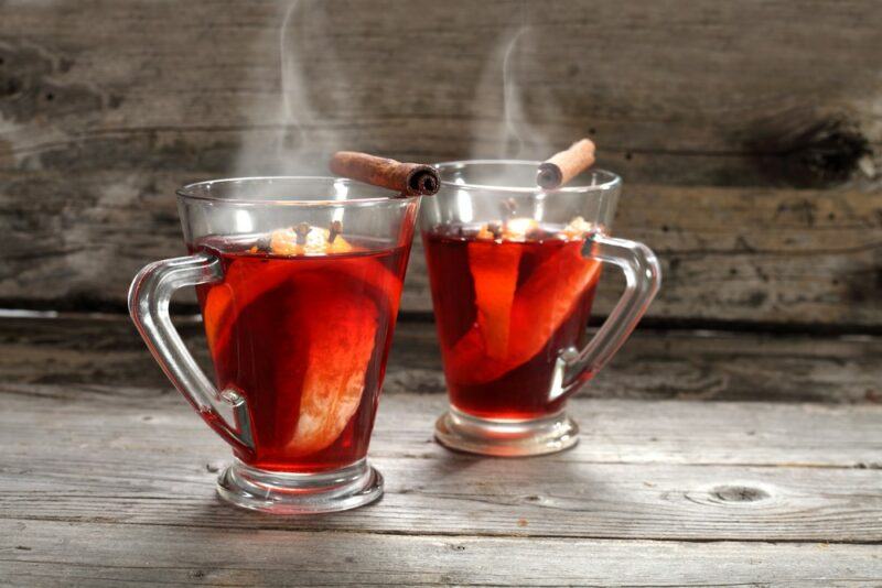 Two large glass mugs of mulled wine, in front of a wooden wall