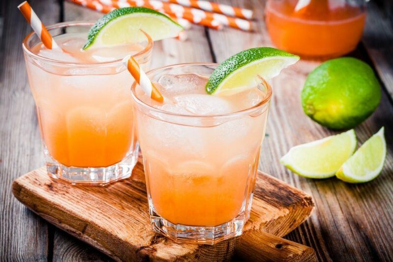 A wooden tray with two glasses of a pink summer shandy, with straws and lime wedges