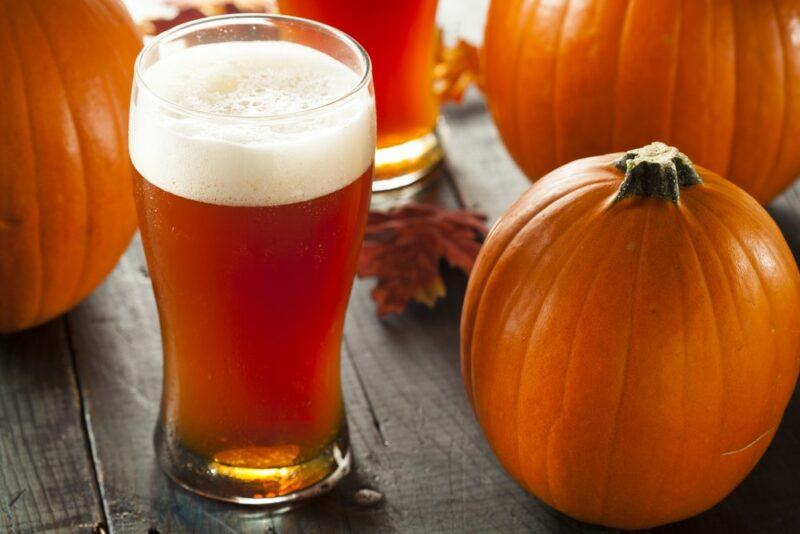 Two pint glasses of pumpkin ale, plus three pumpkins on the table