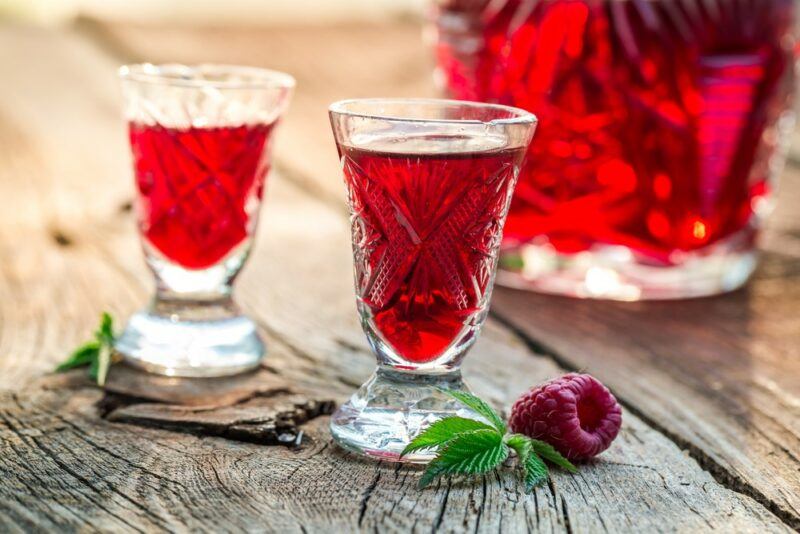 A wooden table with two small glasses of raspberry liqueur in front of a large bottle of the liqueur