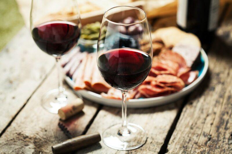 Two glasses of a red beaujolais wine on a wooden table with a plate of cold cuts and nibbles in the background