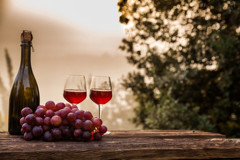 Two glasses of round Italian red wines outside next to a bunch of grapes and a bottle of wine