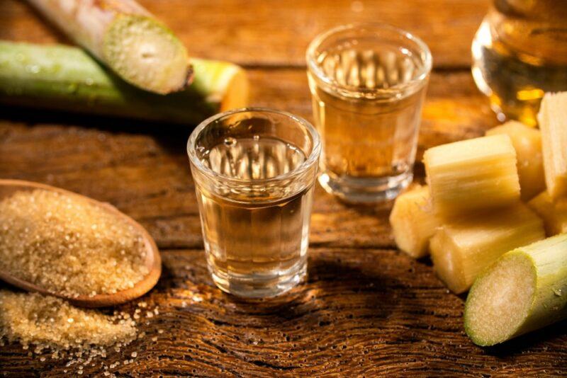 A wooden table with two small shot glasses of rum, next to sugarcane and a spoon of sugar