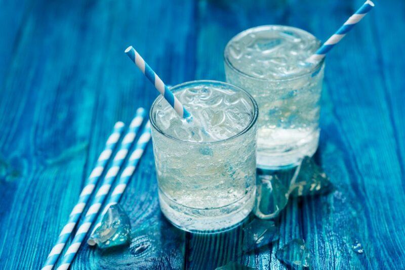 Two glasses of sparking water on a blue table, with blue and white straws and a few more straws on the table