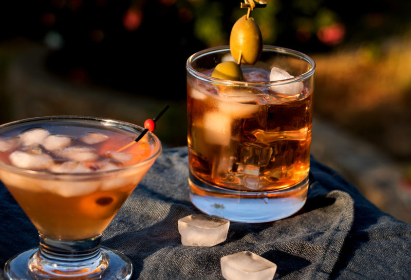 A wooden table with two different shaped glasses of sweet red vermouth on the rocks