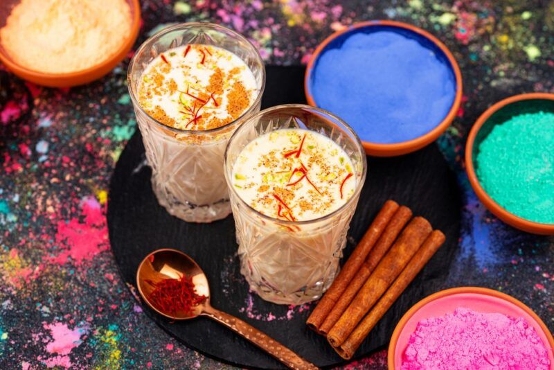 Two glasses of thandai with small bowls containing different colored powders