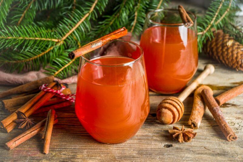 Two glasses of hot wassail next to cinnamon sticks