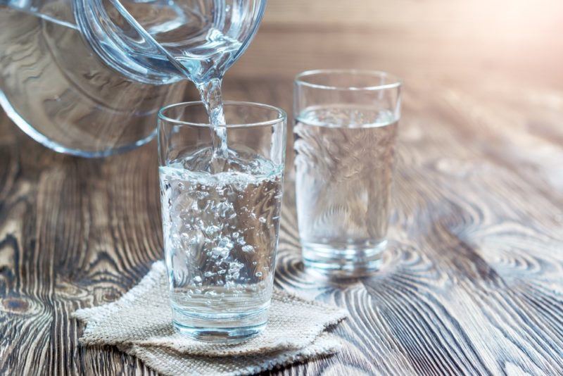 Two glasses of water on a table, with one being poured from a jug