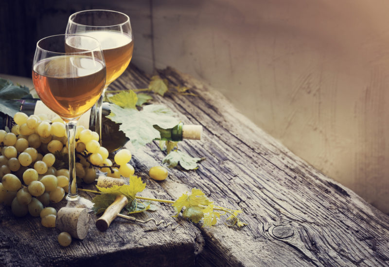 A wooden table with two glasses of white burgundy wine and some grapes