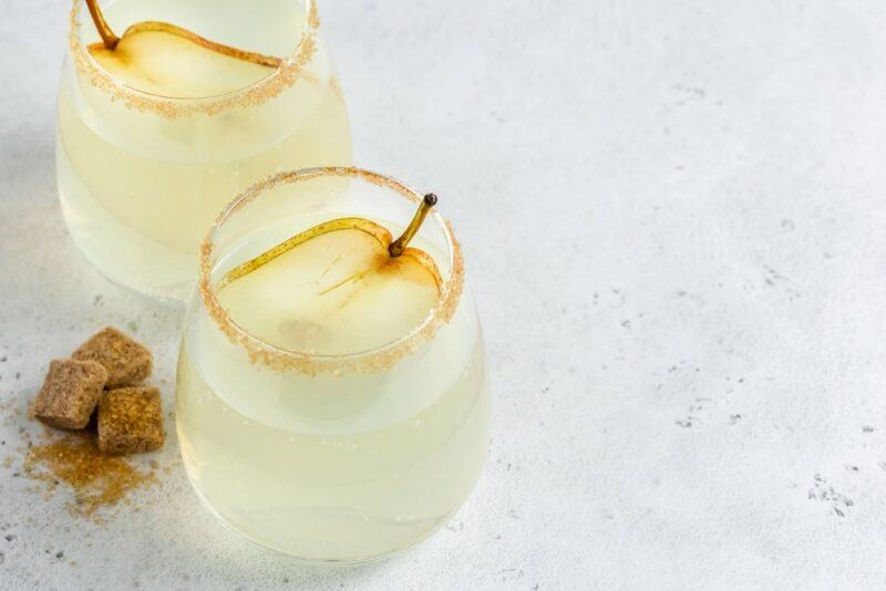 Two glasses of a pear mulled gin cocktail on a marble table with a few cubes of brown sugar