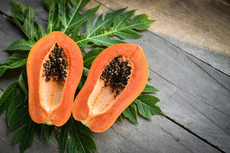 Two halves of a papaya against leaves from the tree