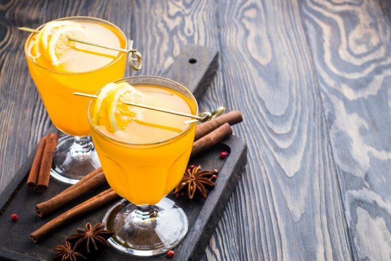 Two glasses containing hot toddies next to some long cinnamon sticks on a wooden tray