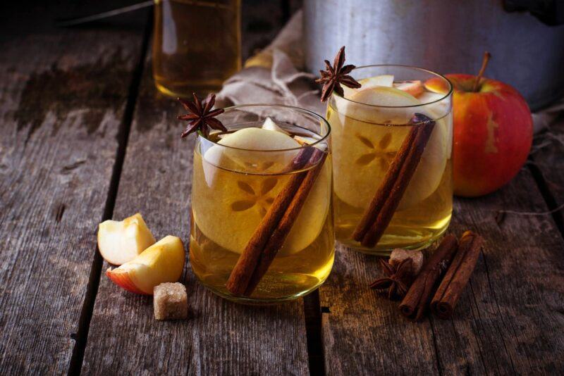 Two glasses containing hot toddies garnished with cinnamon sticks, apple slices, and star anise