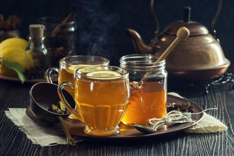 Two mugs of a Fireball hot toddy, with a container of honey on a wooden tray