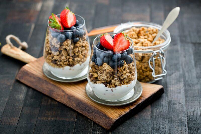 Two jars of granola parfait with yogurt and fruit, with more granola in the background