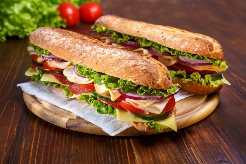 A wooden board with two large subway sandwiches with lettuce, tomatoes, and other fillings