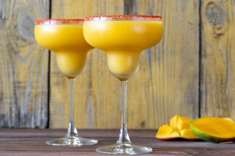 Two White Claw mango margarita cocktails in traditional margarita glasses, rimed with a spice mix