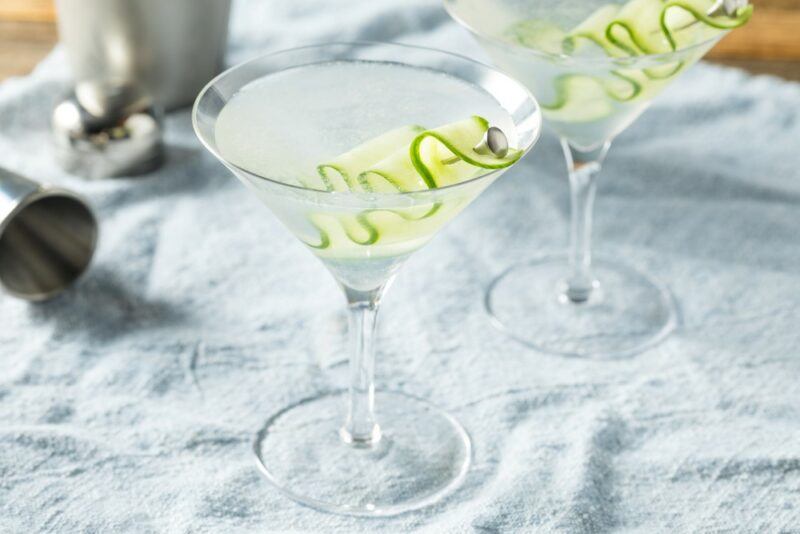 Two martini glasses containing a saketini cocktail garnished with a strip of cucumber