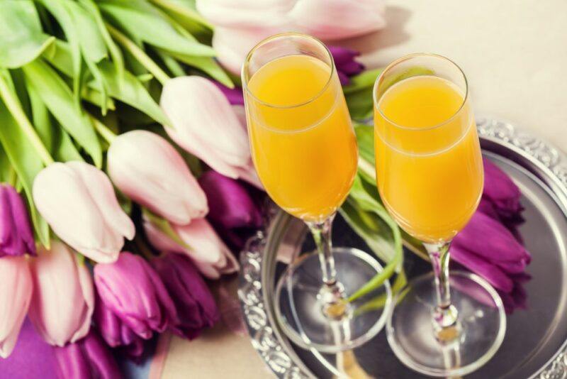 A metal tray of two mimosas next to purple and white tulips