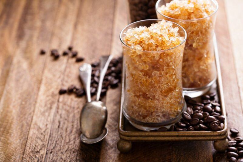 Two glasses filled with a mocha snow cone, on a tray next to a selection of coffee beans