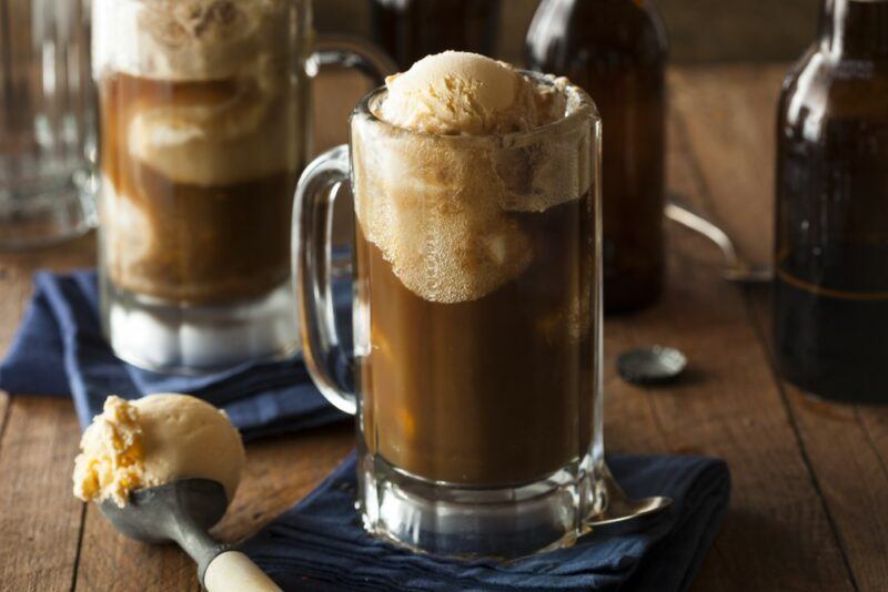 Two large mugs containing a Guinness float with vanilla ice cream, next to a scoop of ice cream on the table