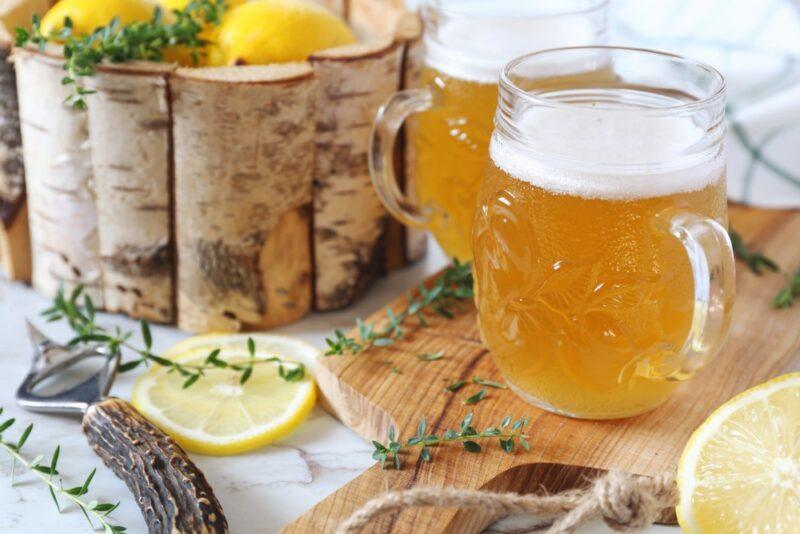 A wooden table with two mugs of shandy and a container of lemons