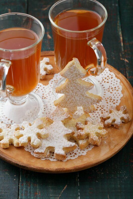 A wooden tray with two mugs of a gingerbread cocktail and various pieces of shortbread