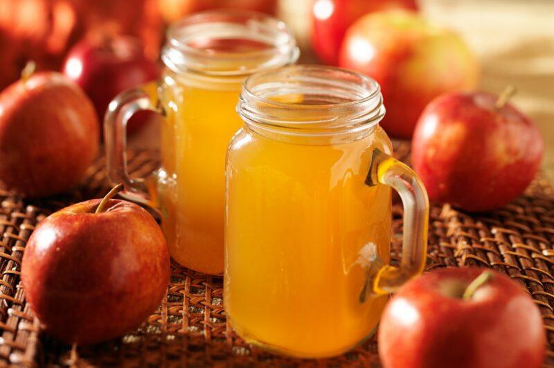 Two mason jars filled with apple pie moonshine, surrounded by fresh apples