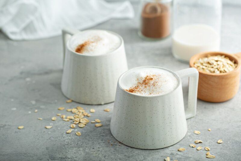 Two mugs of coconut milk foamy coffee on the table, with sugar scattered around and some bowls in the background