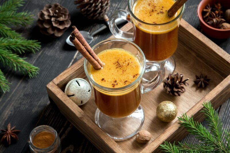 A wooden tray with two glasses of hot buttered rum, with Christmas decorations