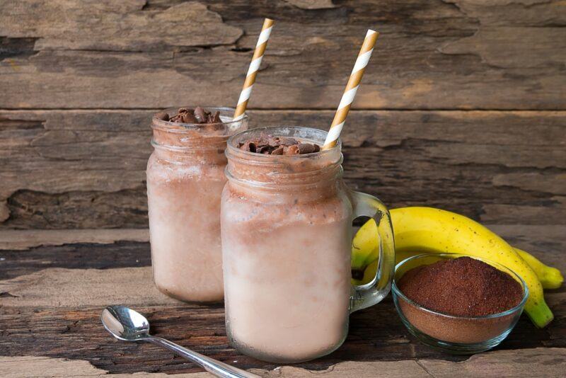 Two mason jars filled with chocolate protein shake, next to a banana and some cocoa powder