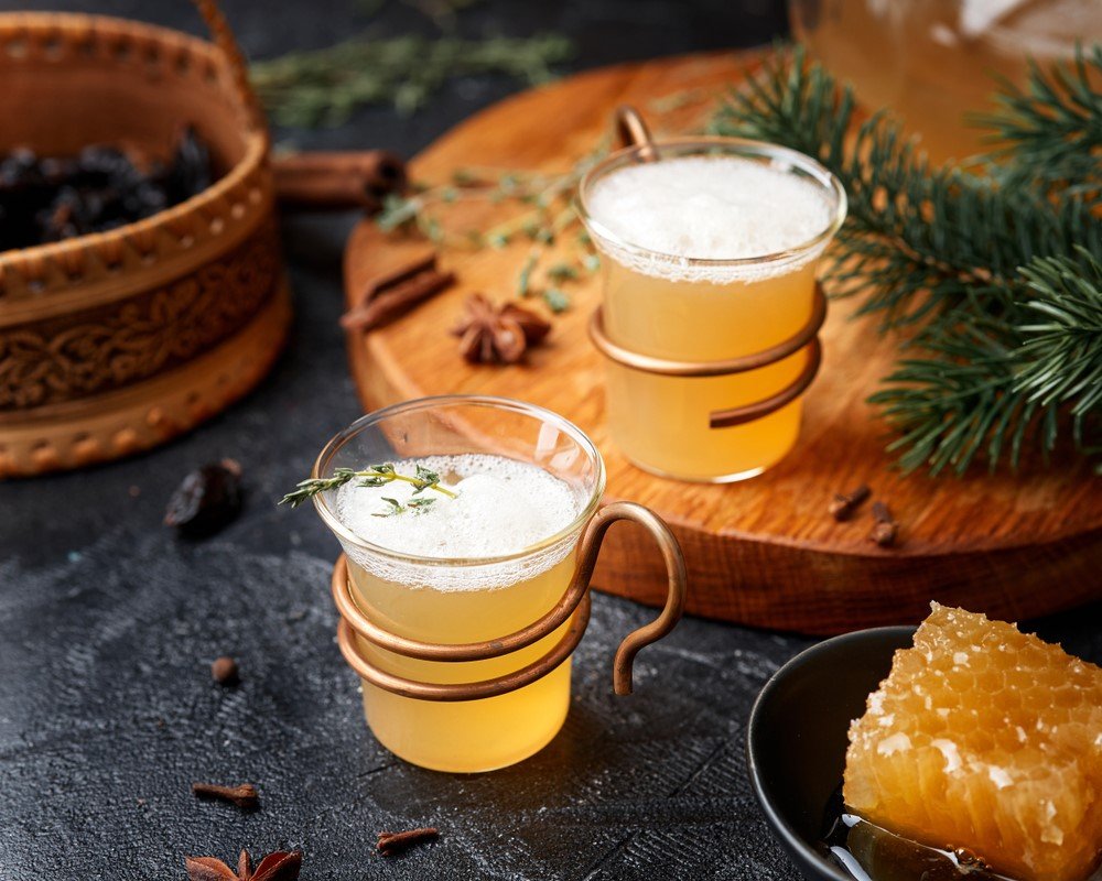 Two glass mugs of sbiten on a wooden board and a black table