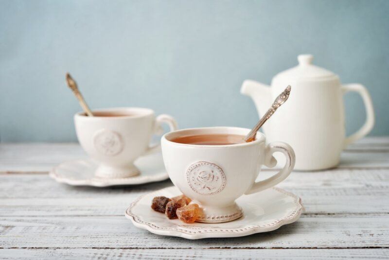 Two white cups of tea with spoons on saucers, in front of a white mug of tea