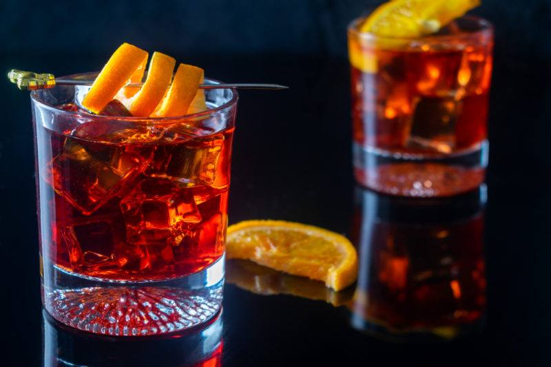 Two negroni cocktails isolated on black. One is garnished with a citrus twist and the other with a citrus wedge