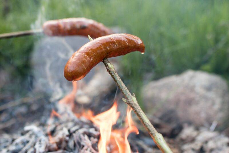 Two people cooking hot dogs over a fire using sticks