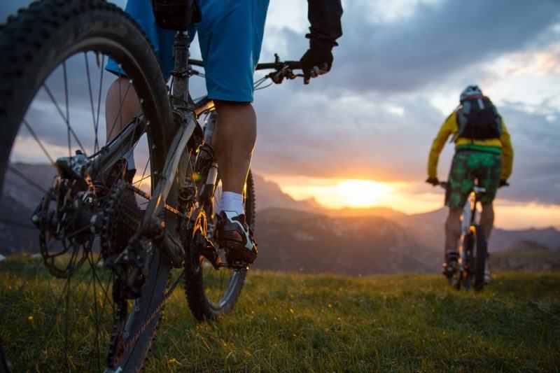 Two people on their mountain bikes riding into the sunset or sunrise