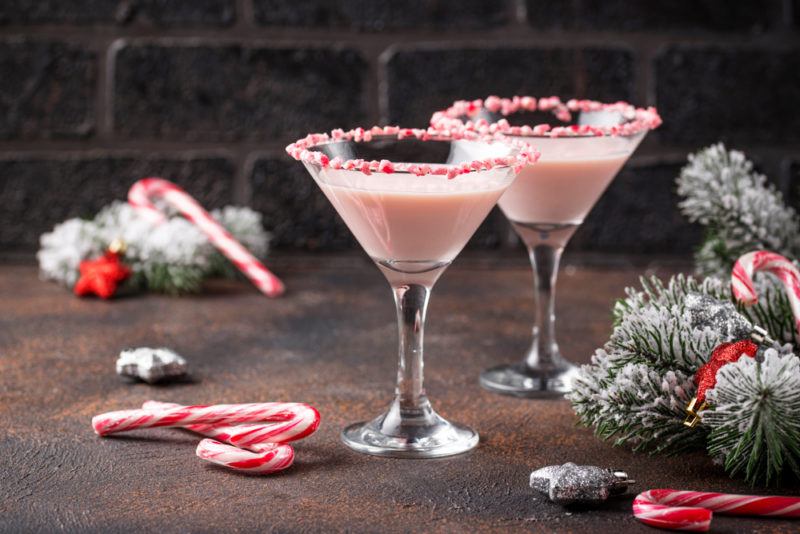 Two martini glasses containing peppermint martinis. There are Christmas tree branches and candy canes scattered across the table