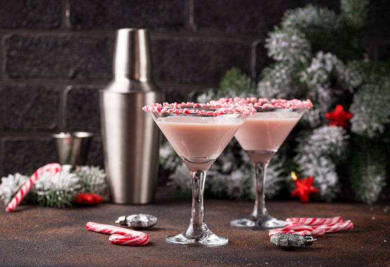 Two peppermint martinis on a wooden table next to a cocktail shaker