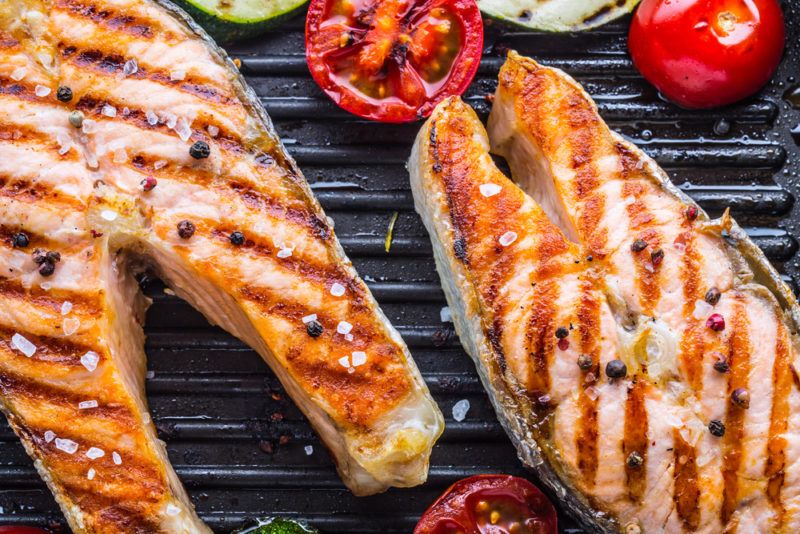 Two salmon steaks on a grill with a few tomatoes