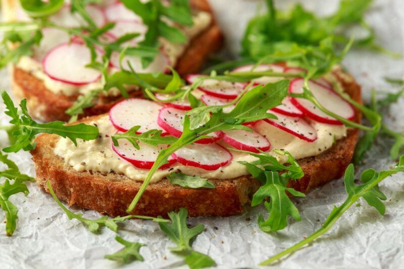 Two slices with toasted sourdough, that has been topped with hummus, sliced radishes, and rocket