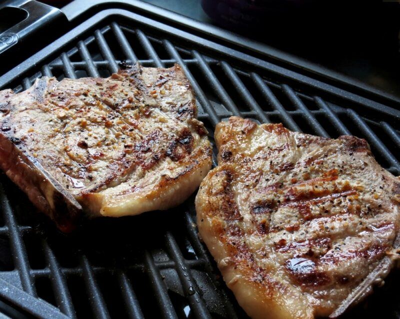 A black indoor grill with two pieces of steak cooking